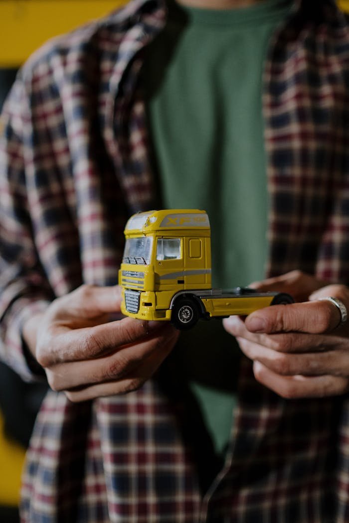 Detailed shot of hands holding a small yellow toy truck against a blurred background.